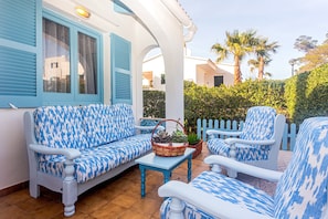 A patio with a blue and white patterned sofa, a matching armchair, and a small table with a basket of plants. - Charming Vacation Home “Villa Arbocers” with Wi-Fi, A/C, Terrace & Garden; Parking Available (Ciutadella de Menorca)