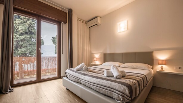 Une chambre avec un grand lit, une table de chevet avec une lampe, une fenêtre avec des rideaux et un appareil de climatisation.