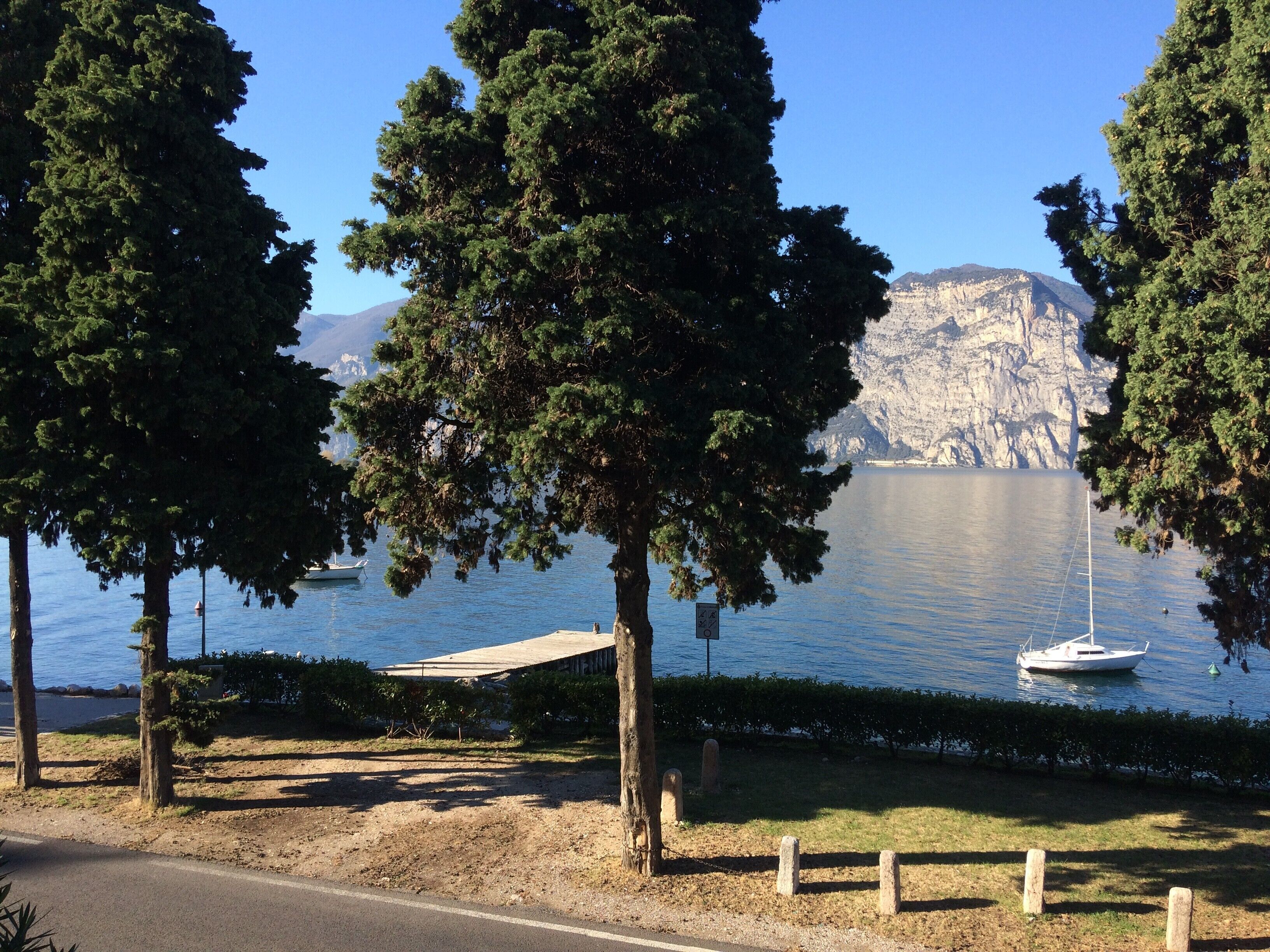 A coastal view with a boat docked near a rocky cliff, trees, and a clear sky.