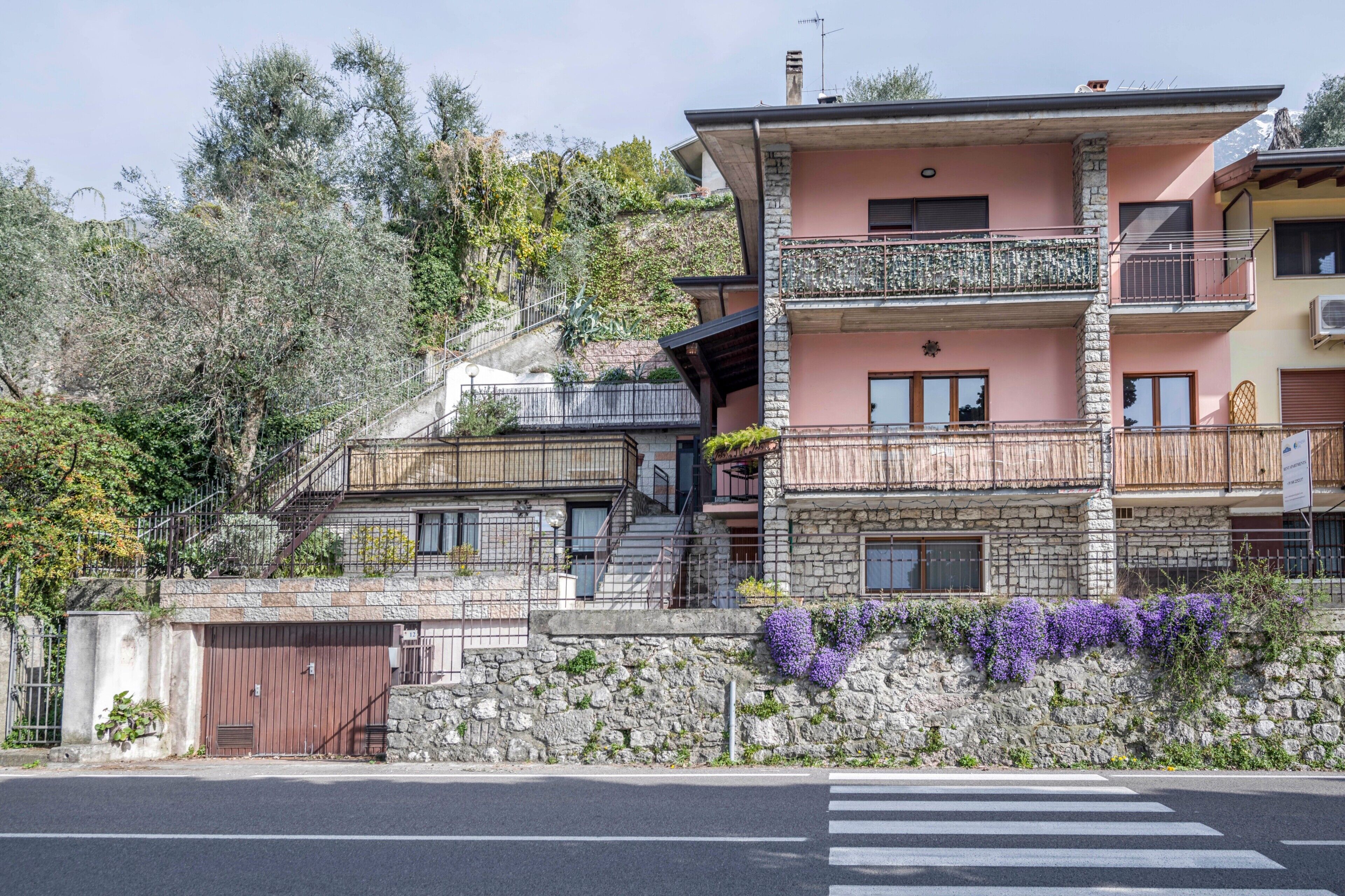A multi-story building with balconies, a stone facade, and a crosswalk in front.