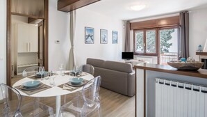 Un salon moderne comprenant un coin repas, un canapé, un téléviseur et une fenêtre donnant sur un beau paysage.