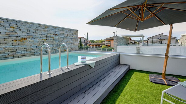 Ein Pool auf dem Dach mit Steinmauern, einer Metallleiter und einem großen Sonnenschirm.
