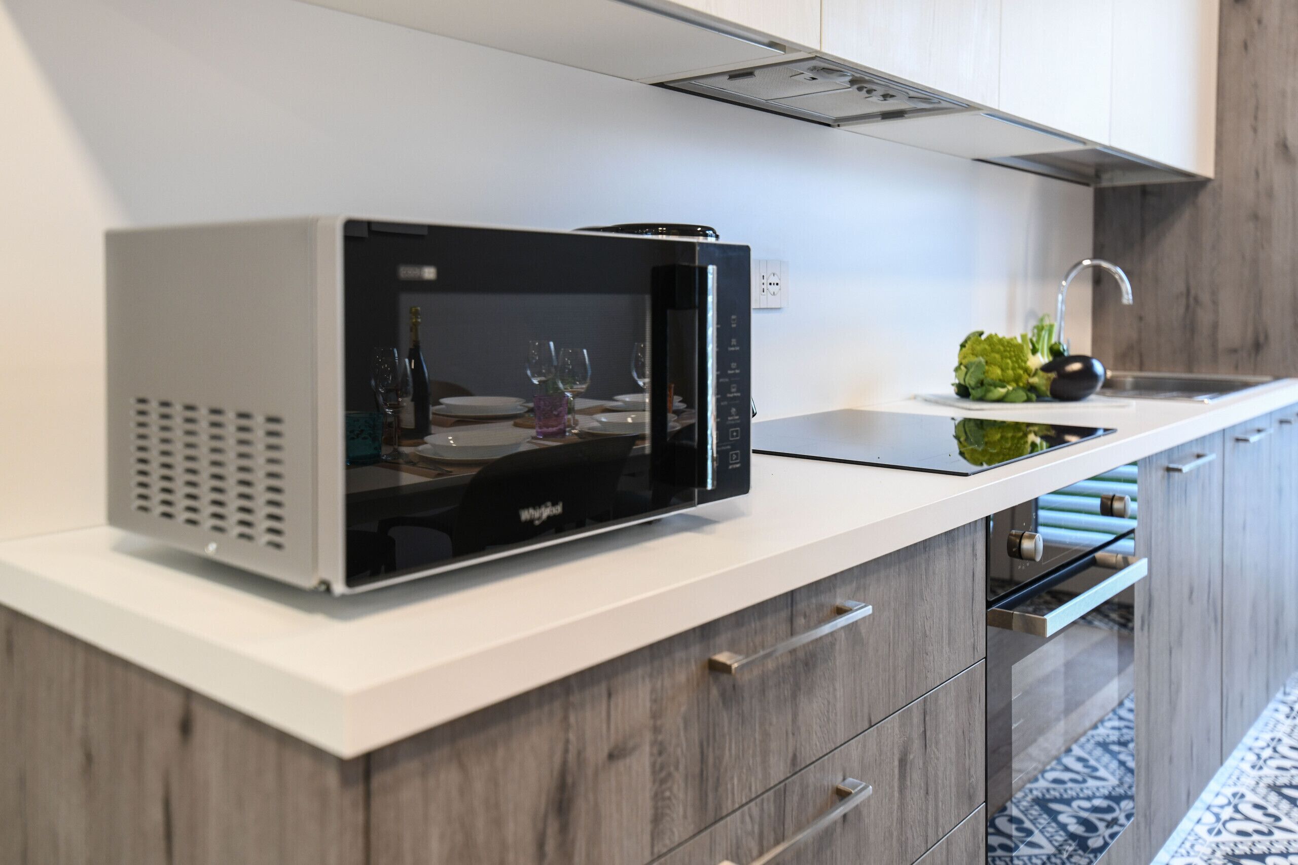 Una cocina con microondas sobre una encimera blanca, un lavabo con grifo y una pequeña planta.