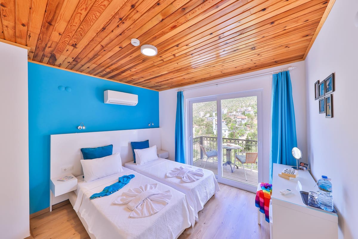 Ein Zimmer mit zwei Betten, einem Schreibtisch und einem Balkon mit blauen Vorhängen.