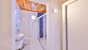 A modern bathroom with a wooden ceiling, a white sink, a toilet, and a glass-enclosed shower area.