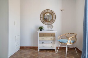 A room with a white cabinet, a wicker chair, and a wall-mounted mirror.