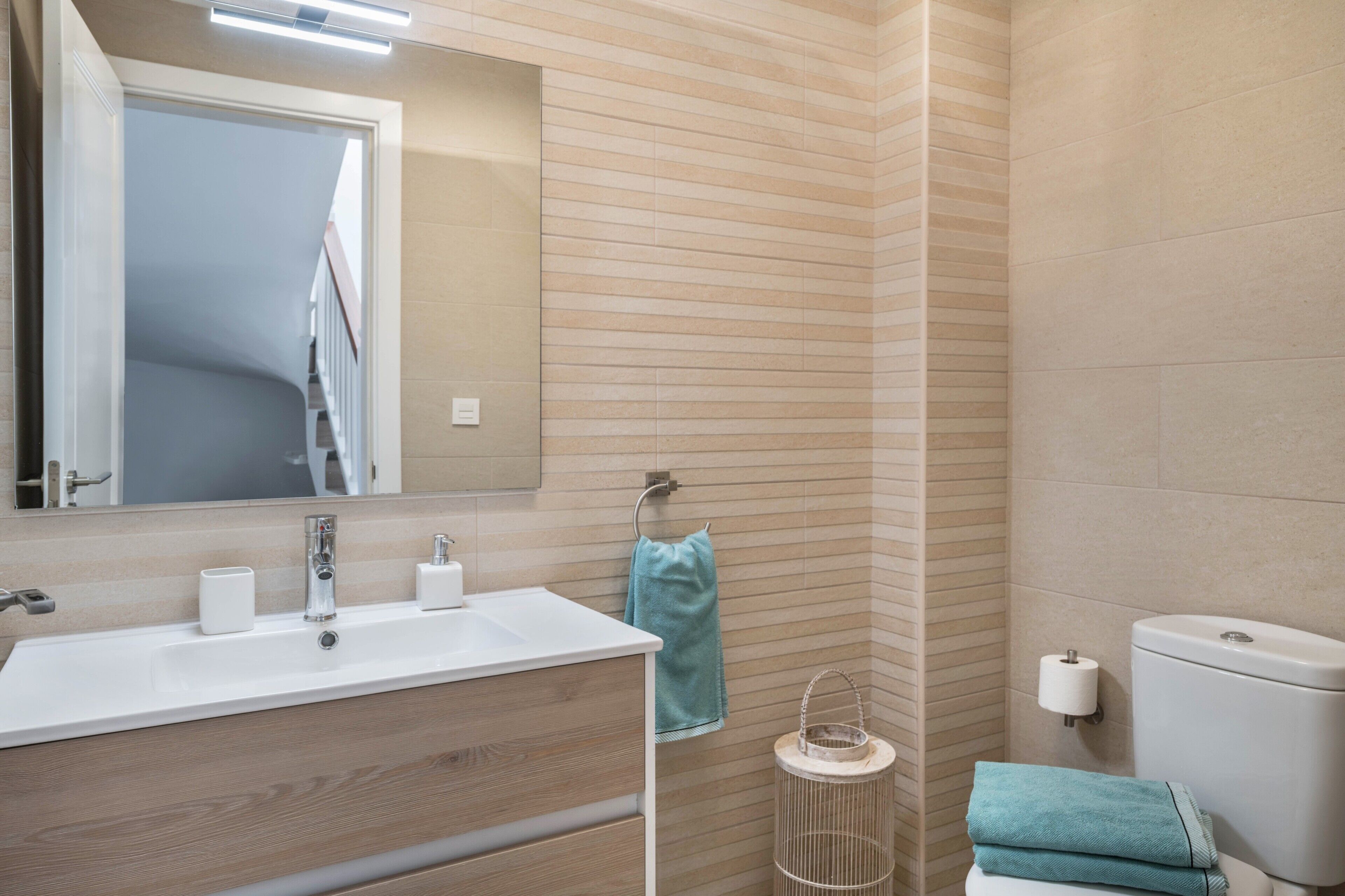 Une salle de bain équipée d’un lavabo, d’un miroir, d’un porte-serviettes, de toilettes et d’une petite poubelle ronde.