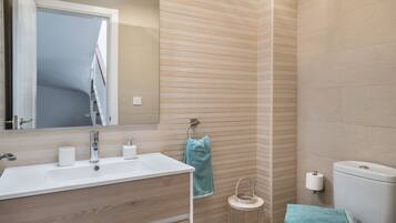 Une salle de bain équipée d’un lavabo, d’un miroir, d’un porte-serviettes, de toilettes et d’une petite poubelle ronde.