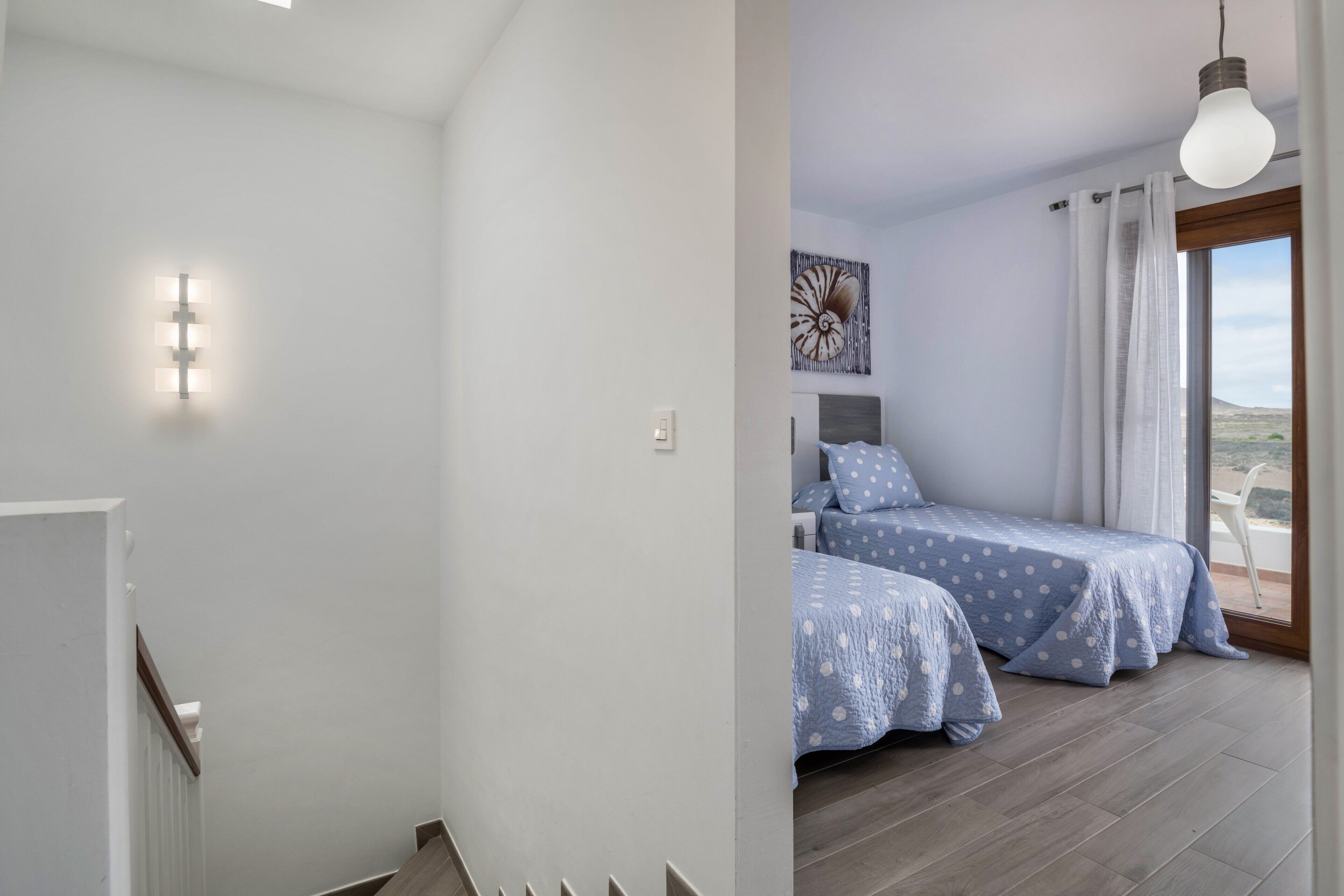 Un dormitorio con dos camas, una lámpara en el techo, un cuadro y vistas a través de una ventana.