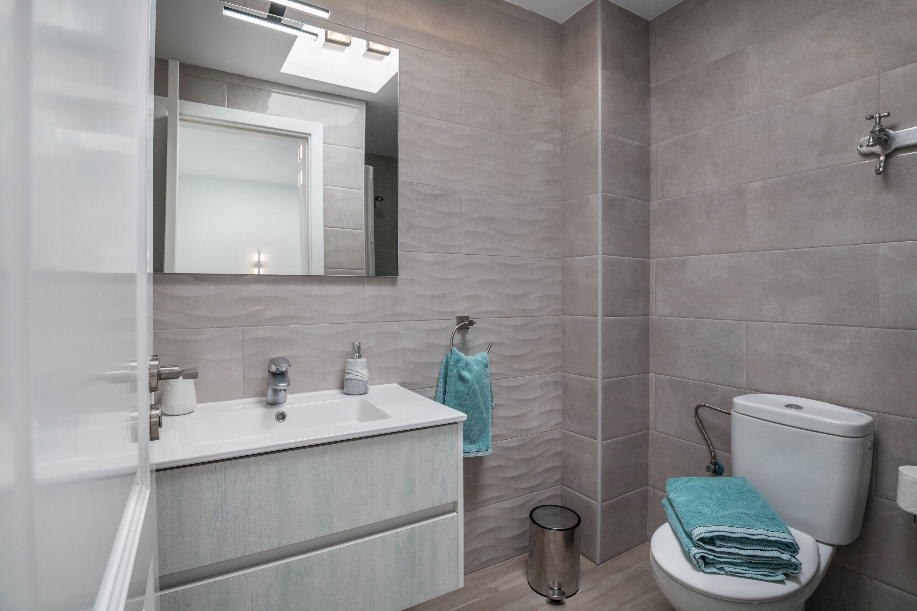 Une salle de bain moderne équipée d’un lavabo, d’un miroir, de toilettes et d’une poubelle.