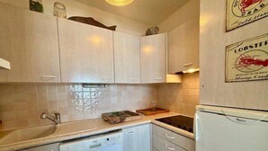 Une cuisine avec des meubles blancs, un lave-vaisselle, un réfrigérateur et un dosseret carrelé.