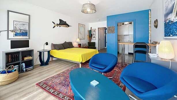 Une chambre d’hôtel moderne avec un lit, deux chaises bleues, une petite table, un téléviseur et une bibliothèque.