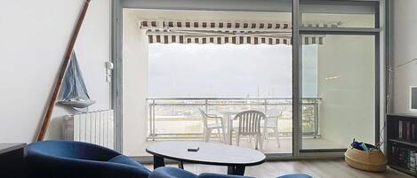 Uma sala de estar moderna com uma grande porta de vidro deslizante que dá para uma varanda com vista para o horizonte da cidade.