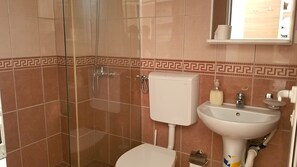 A bathroom with a glass shower enclosure, a toilet, and a sink with a soap dispenser. - Hotel La Rosa Negra (Ulcinj)