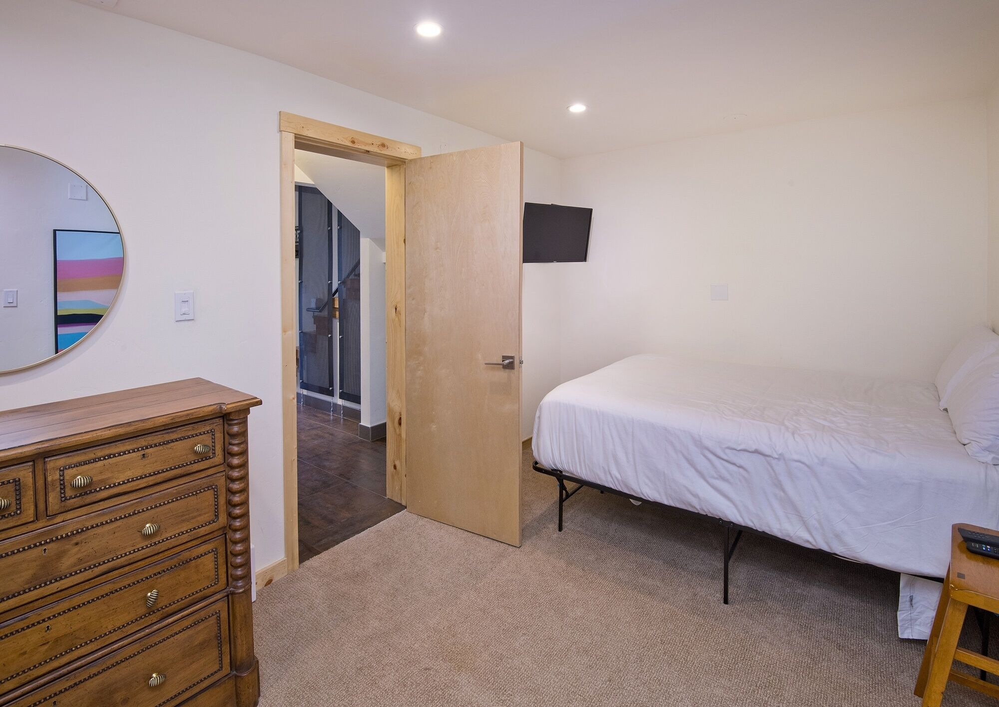 Un dormitorio con una cama, un aparador de madera, un espejo y una puerta que da a otra habitación.