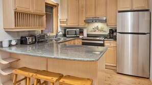 A kitchen with wooden cabinets, a stainless steel refrigerator, a microwave, a toaster, and two wooden stools. - Eiger 9 3 Bedroom Condo by RedAwning (Vail)