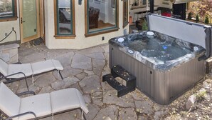 An outdoor hot tub area with stone flooring, lounge chairs, and a wooden deck. - Eiger 9 3 Bedroom Condo by RedAwning (Vail)