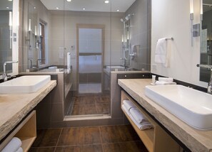 Un baño moderno con dos lavamanos, una ducha con cerramiento de vidrio y un espejo grande.