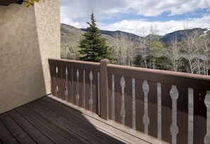 Una terraza de madera con barandilla, con vista a un paisaje montañoso con árboles y casas.