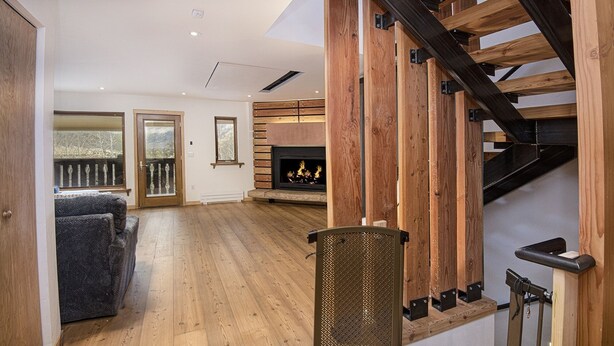 A spacious living area with a wooden floor, a fireplace, and a staircase with exposed beams. - Eiger 9 3 Bedroom Condo by RedAwning (Vail)