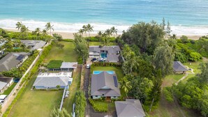 An aerial view of a residential area with houses, a swimming pool, and a beach.