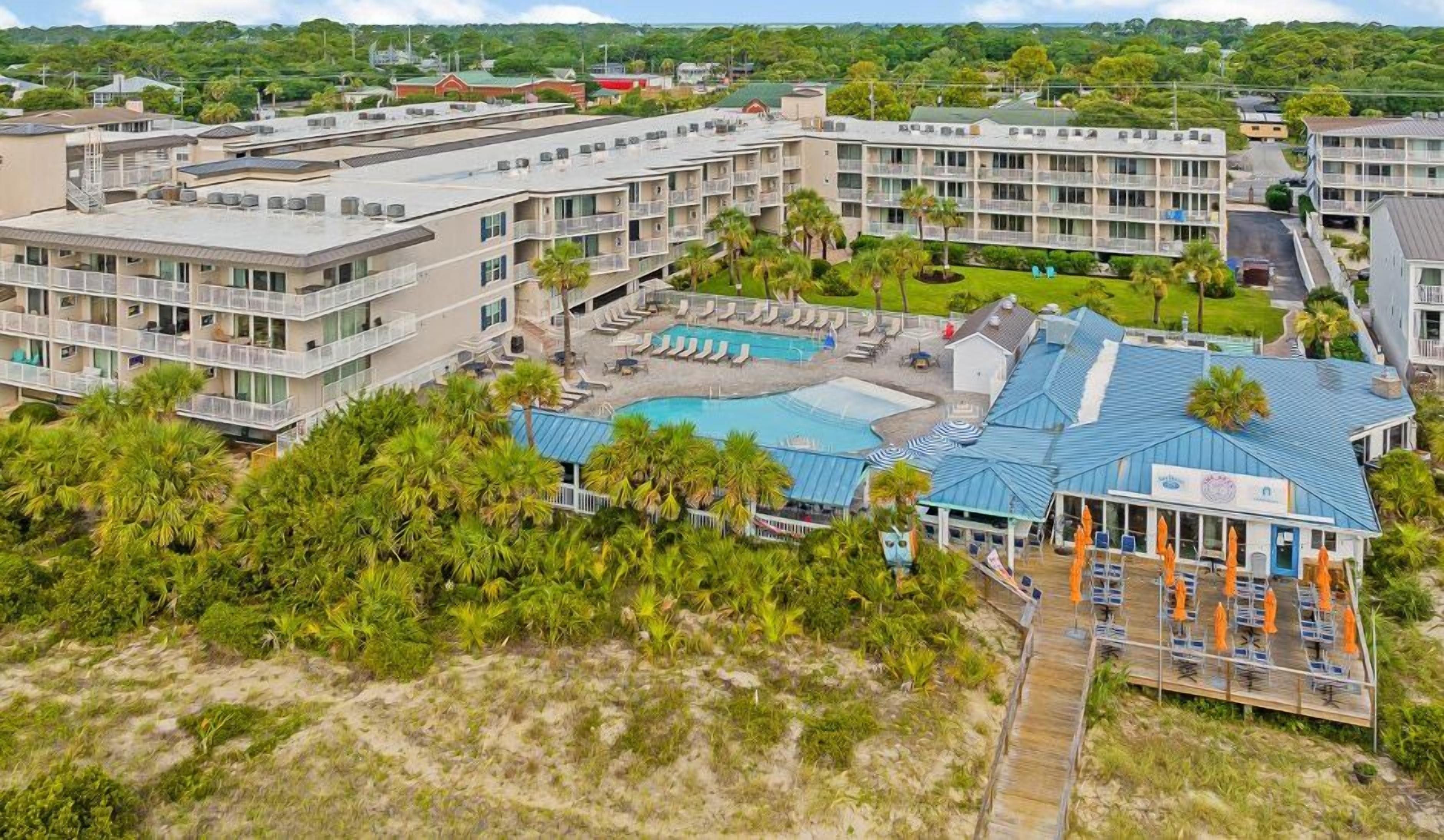 A hotel with multiple floors, a swimming pool, and a beach area with umbrellas.