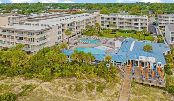 Un hotel con varias plantas, piscina y zona de playa con sombrillas.