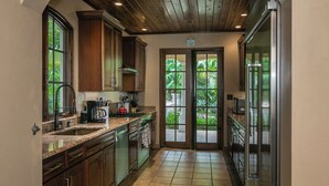 Cocina con armarios de madera, encimeras de granito, refrigerador de acero inoxidable y vistas al exterior a través de la puerta de vidrio.