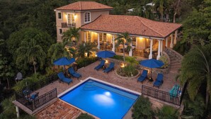Una casa de dos pisos con piscina, mobiliario de exterior y un patio.