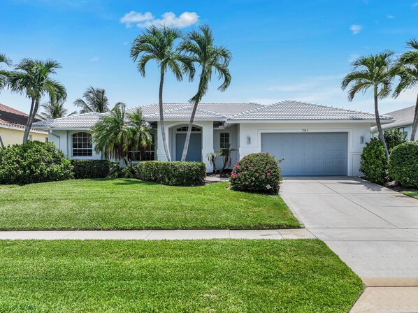 A residential house with a garage, palm trees, and well-maintained lawn.