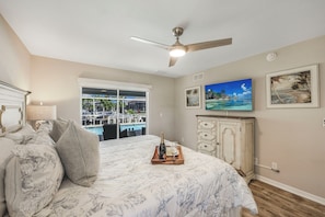 A bedroom with a bed, a ceiling fan, a TV, a window with a view of a pool, and a cabinet.