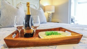 En säng med ett träbricka som innehåller en flaska Brut Cuvée-champagne, två glas och en tallrik med ost och vindruvor.