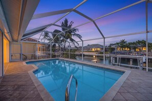 Une piscine entourée de parois en verre, des palmiers et une vue imprenable sur le coucher de soleil.