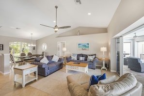 A spacious living room with a ceiling fan, a dining area with a table and chairs, and a large window with a view.