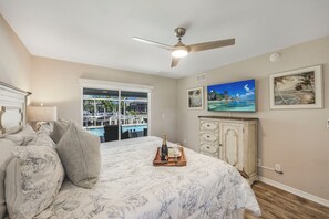 A bedroom with a bed, a ceiling fan, a TV, a window with a view of a pool, and a cabinet.