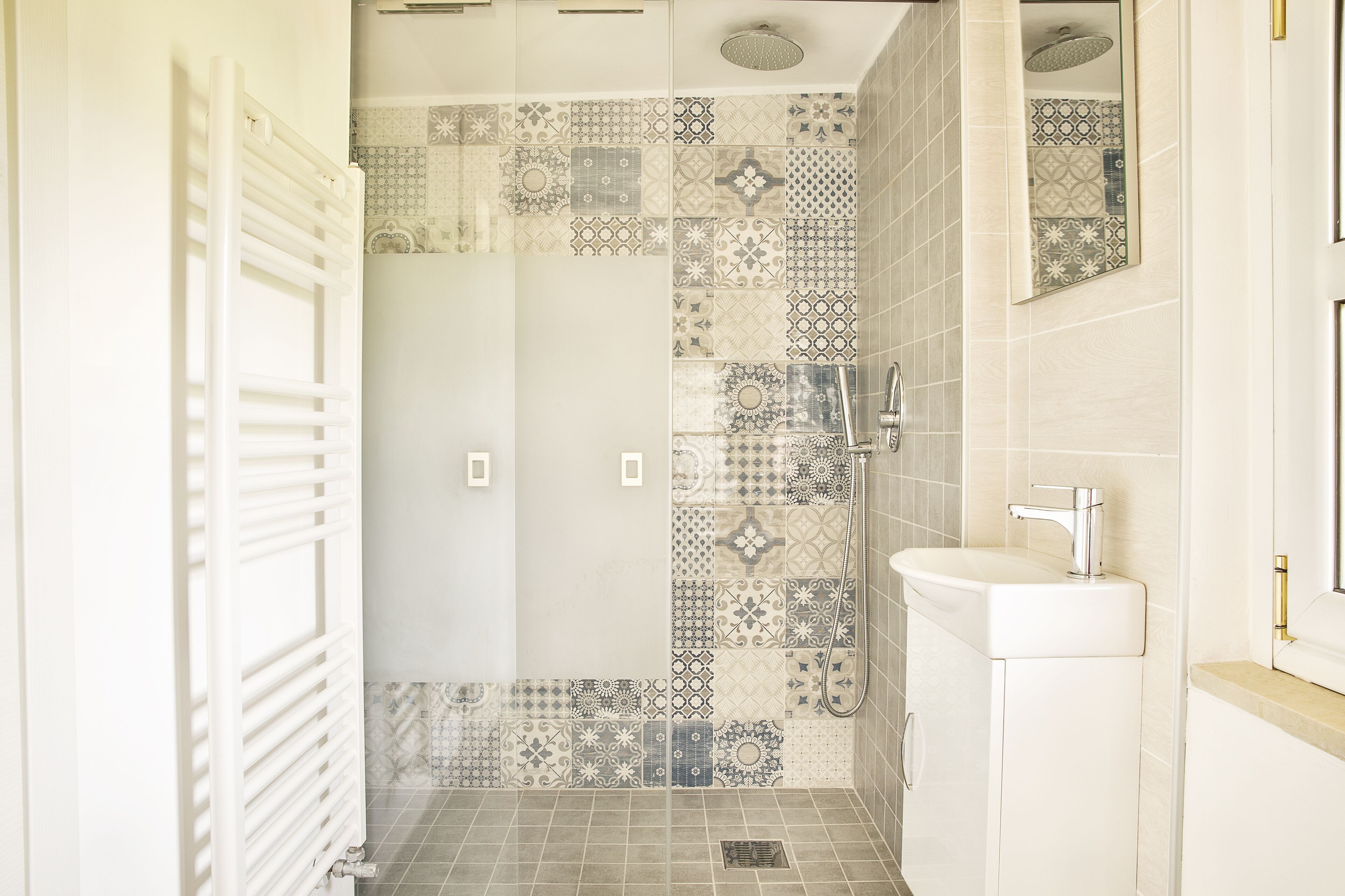 Ein Badezimmer mit Dusche, Waschbecken und einer Wand mit verschiedenen Fliesenmustern.