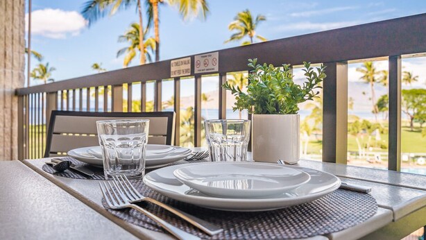 Una mesa servida con platos, vasos y cubiertos, con vista a una piscina rodeada de palmeras.