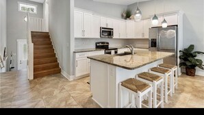 A modern kitchen with white cabinets, a granite countertop, stainless steel appliances, and a central island with bar stools.