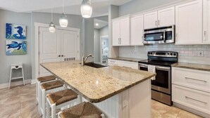A kitchen with white cabinets, a granite countertop, stainless steel appliances, and a bar stool area.