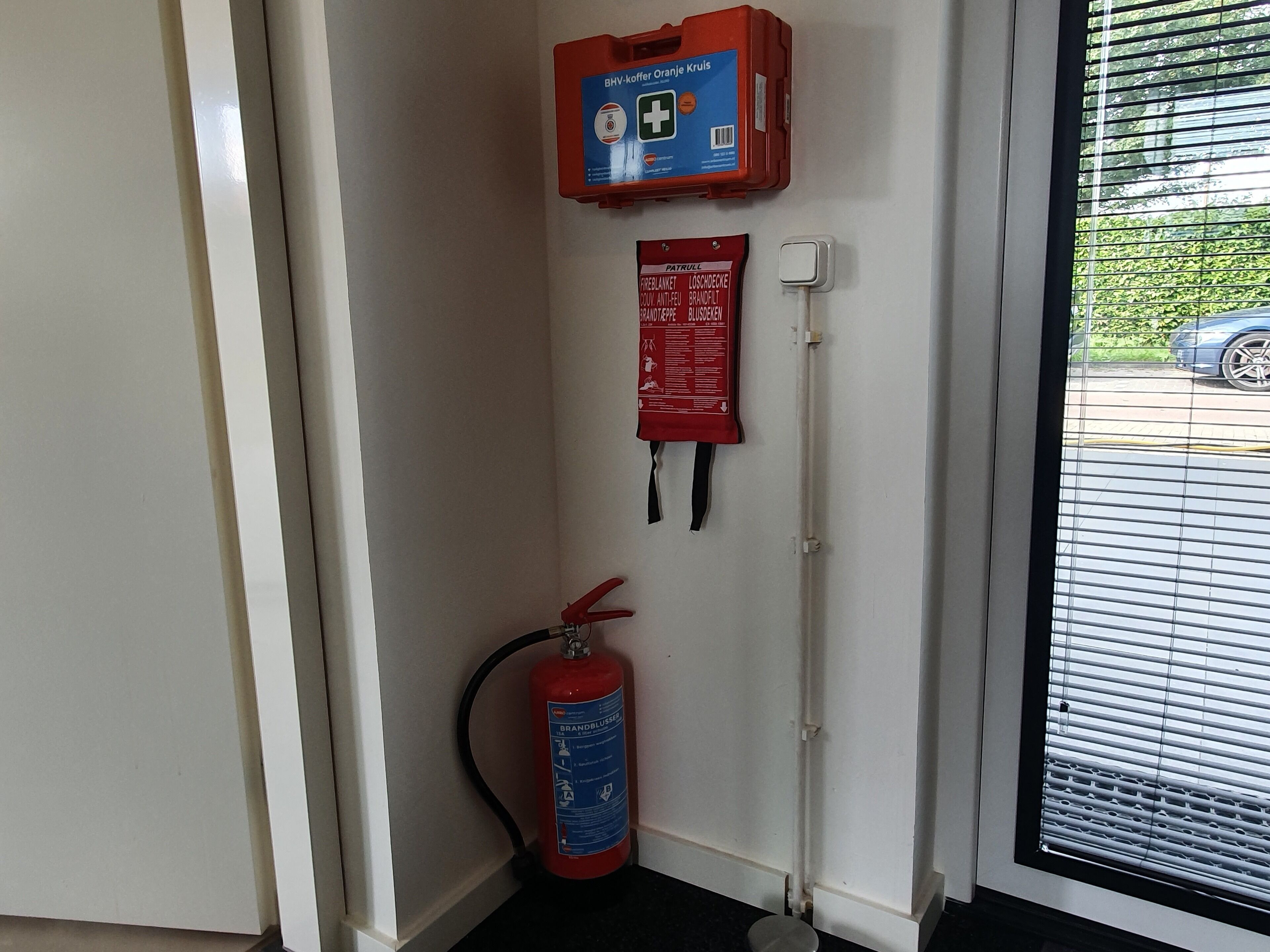 Un extincteur fixé au mur, une trousse de premiers secours et une prise de courant près d’une porte.
