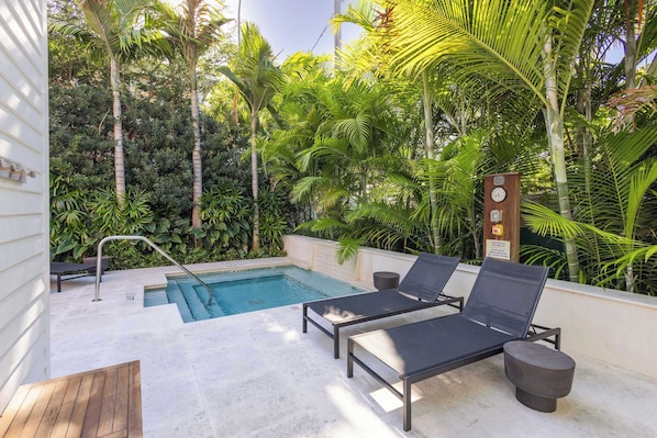 A poolside area with lounge chairs, a pool, and lush greenery.