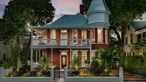 Une maison à deux étages, dotée d’une tour imposante, d’un balcon et d’un jardin bien entretenu.