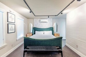 Une chambre d’hôtel avec un grand lit, un banc, une fenêtre et des œuvres d’art accrochées aux murs.