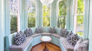 Un coin salon aménagé dans une baie vitrée, avec des coussins à motifs, une table en bois et un lustre.