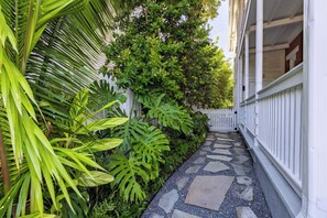 Un étroit sentier de pierres, bordé d’une végétation luxuriante et d’une clôture blanche, mène à un bâtiment doté d’un porche.