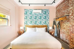 Una habitación de hotel con una cama, un muro de ladrillo, una ventana y un cabecero de madera.