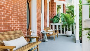 A brick exterior with a wooden bench and a small table with a vase.