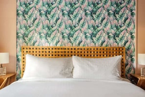A bed with a wooden headboard, white bedding, and a wall with a tropical leaf pattern.