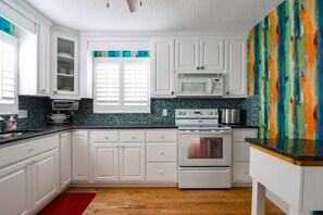 Kitchen features a microwave above the stove, a window with blinds, and a colorful abstract painting.