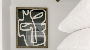 Habitació amb una obra d'art abstracta emmarcada, almoinos blancs i una barra de cortina de fusta.